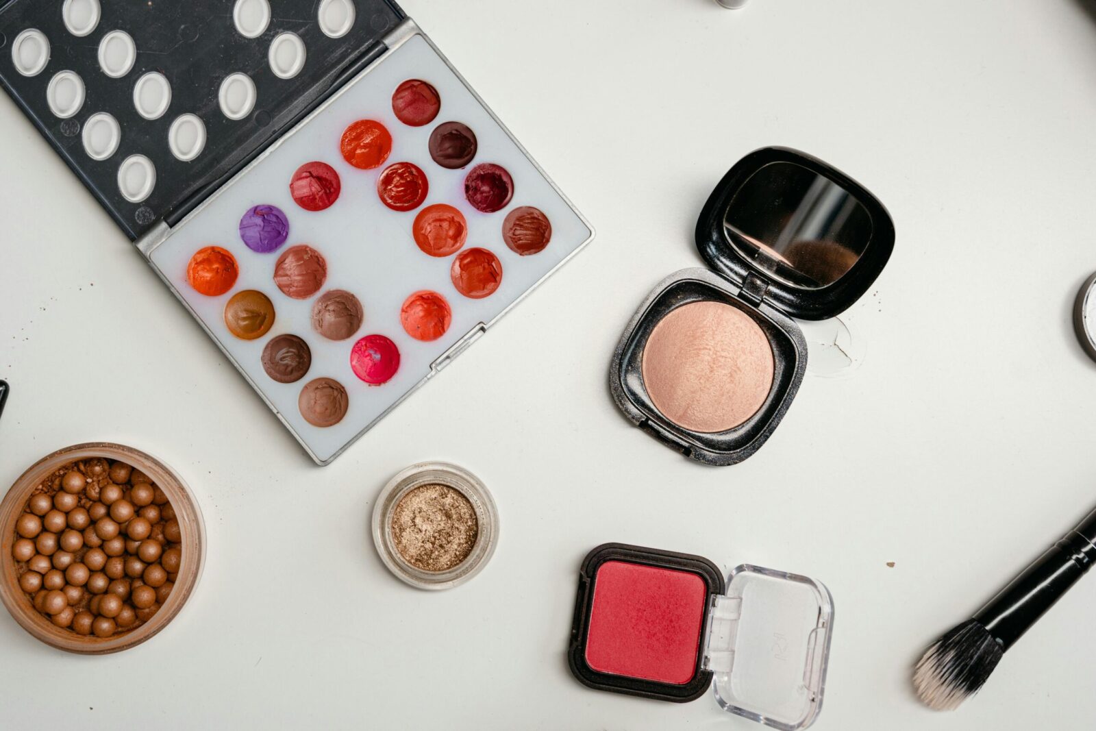 Top view of assorted makeup products including palettes, brushes, and powders on a white surface.